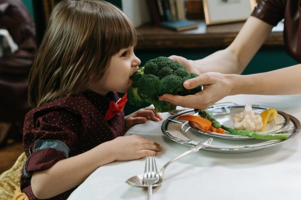pexels-photo-6970101-6970101-1 Cute child eating broccoli, promoting healthy eating habits indoors.